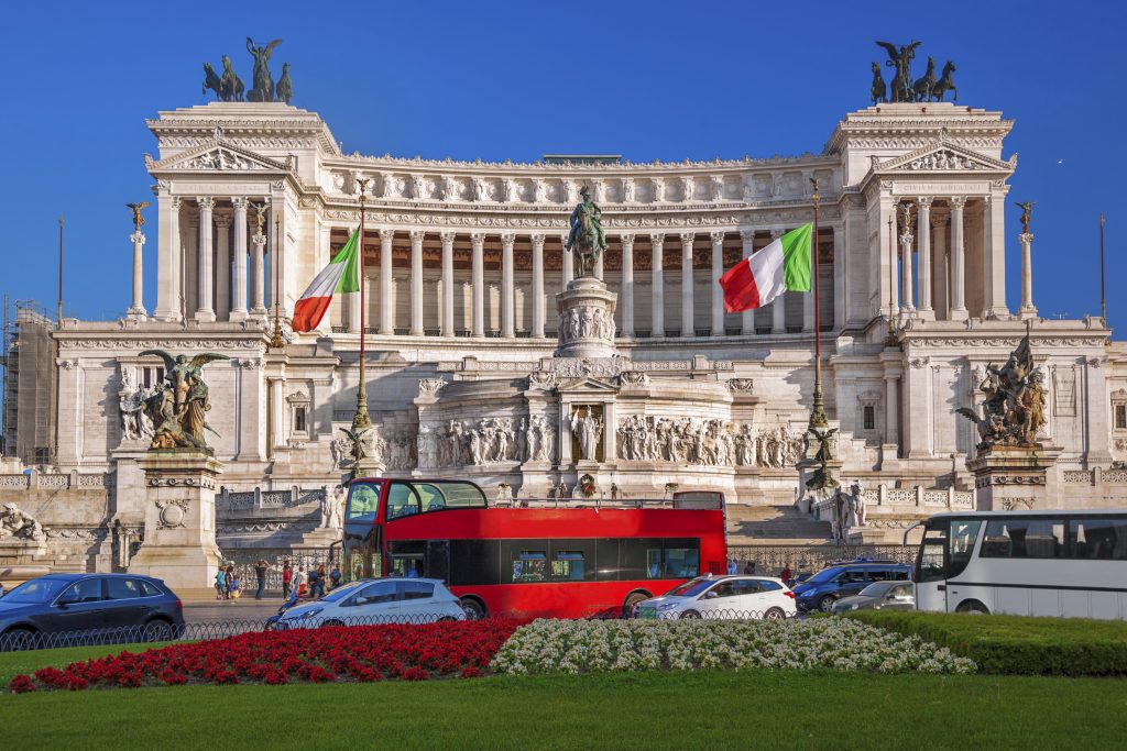 Bus touristique Hop On Hop Off en circulation devant le Monument à Victor-Emmanuel II, offrant une perspective dynamique et historique de Rome.